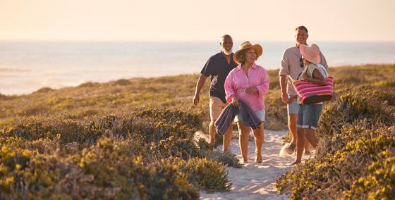Group walking on a beach path with ocean view at sunset.