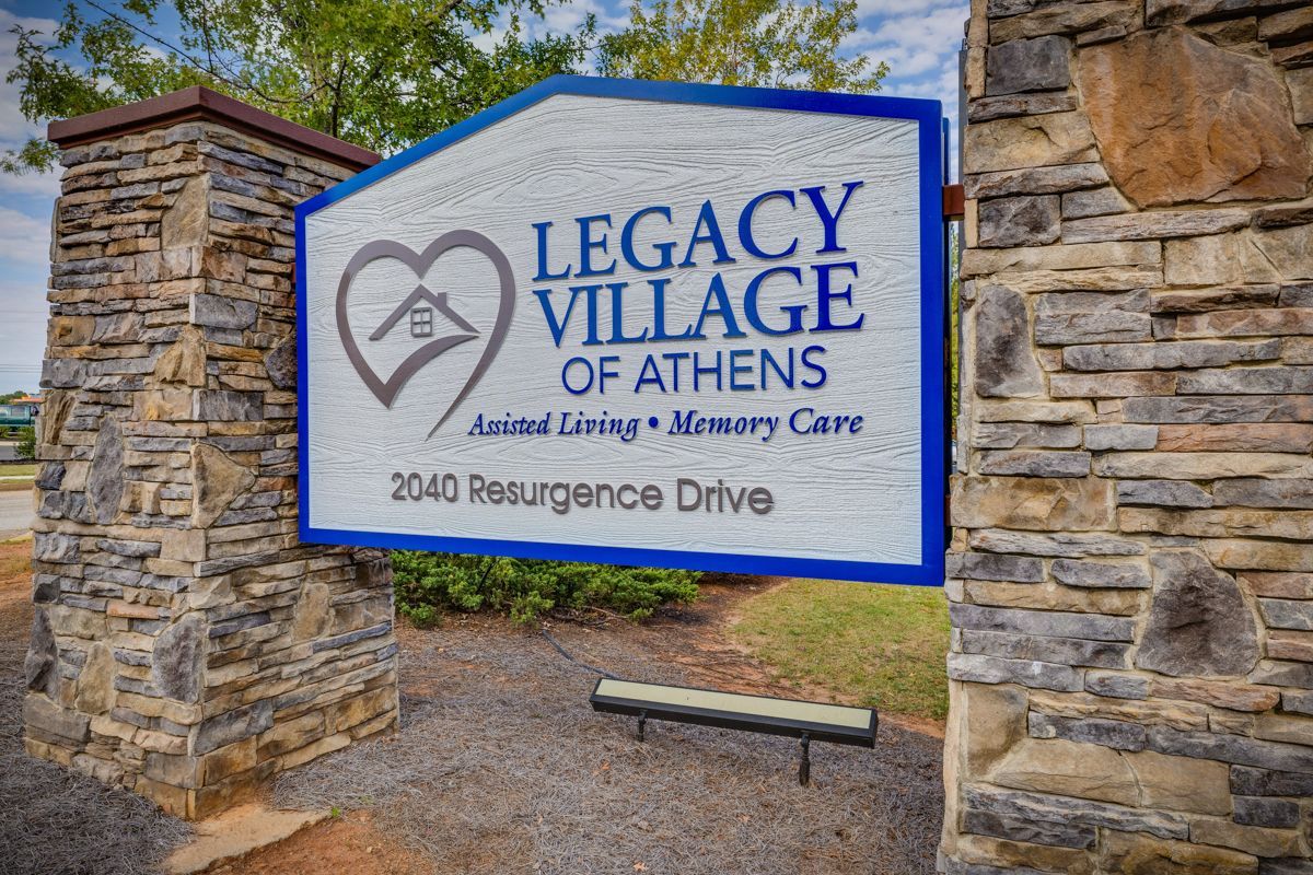 A sign for legacy village of athens is on a stone wall.