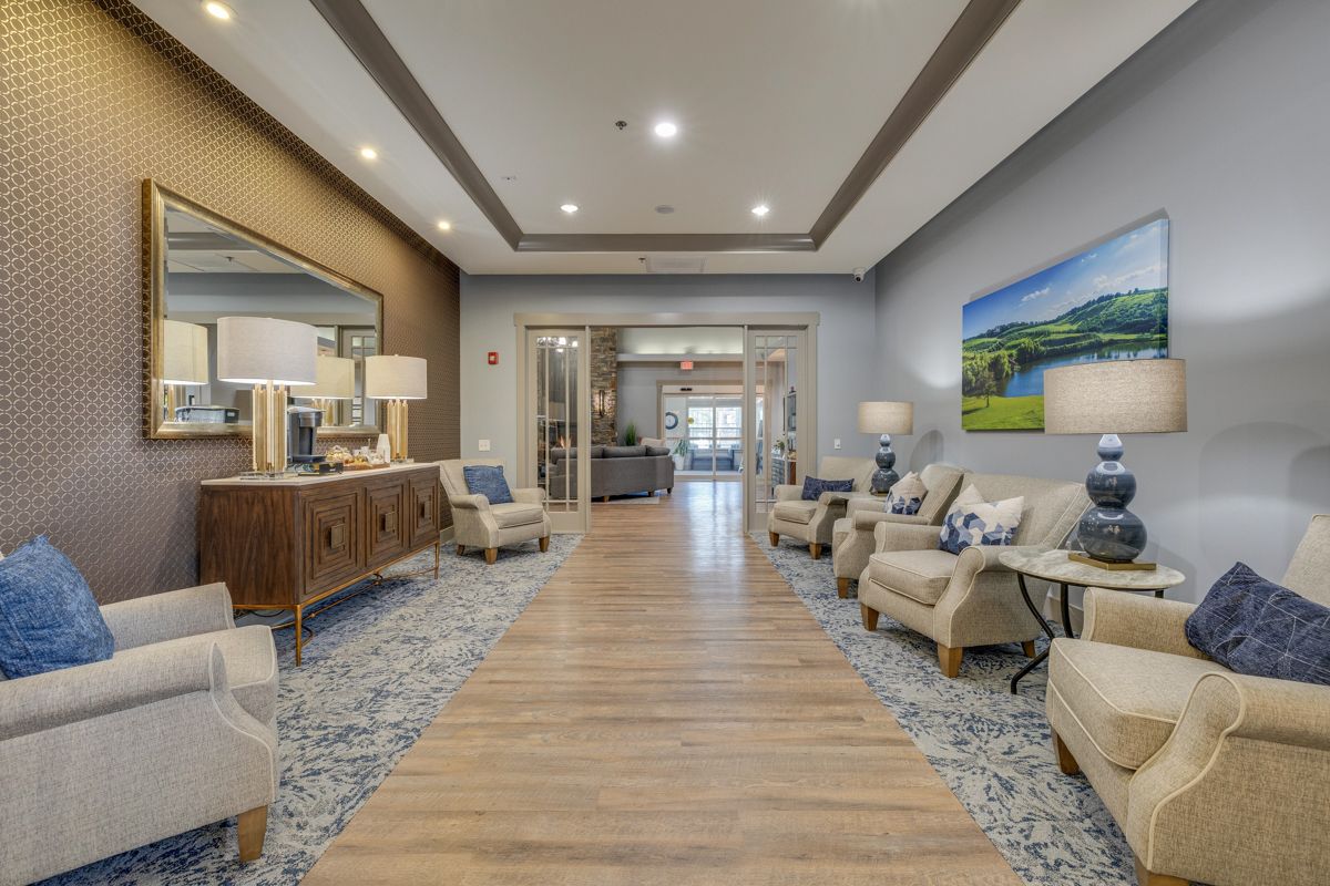 A long hallway filled with chairs , tables , lamps and a mirror.