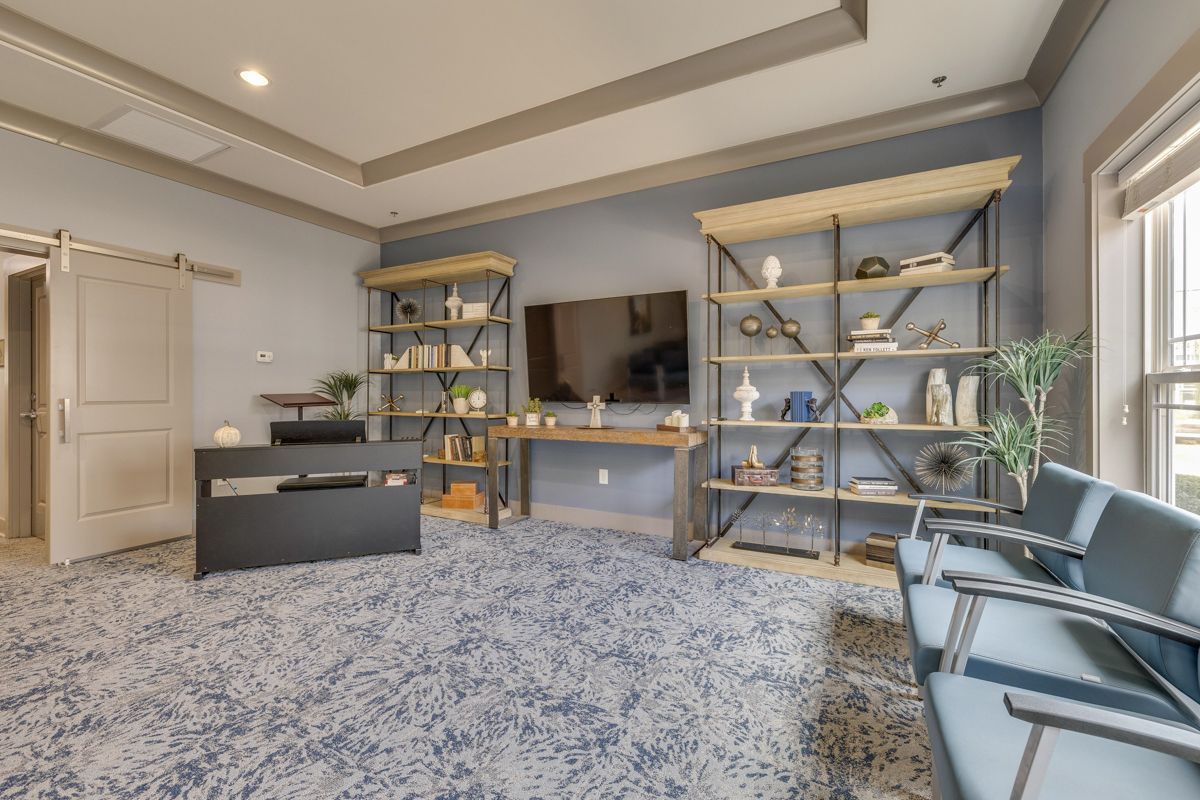 A living room with a desk , chairs , shelves and a flat screen tv.
