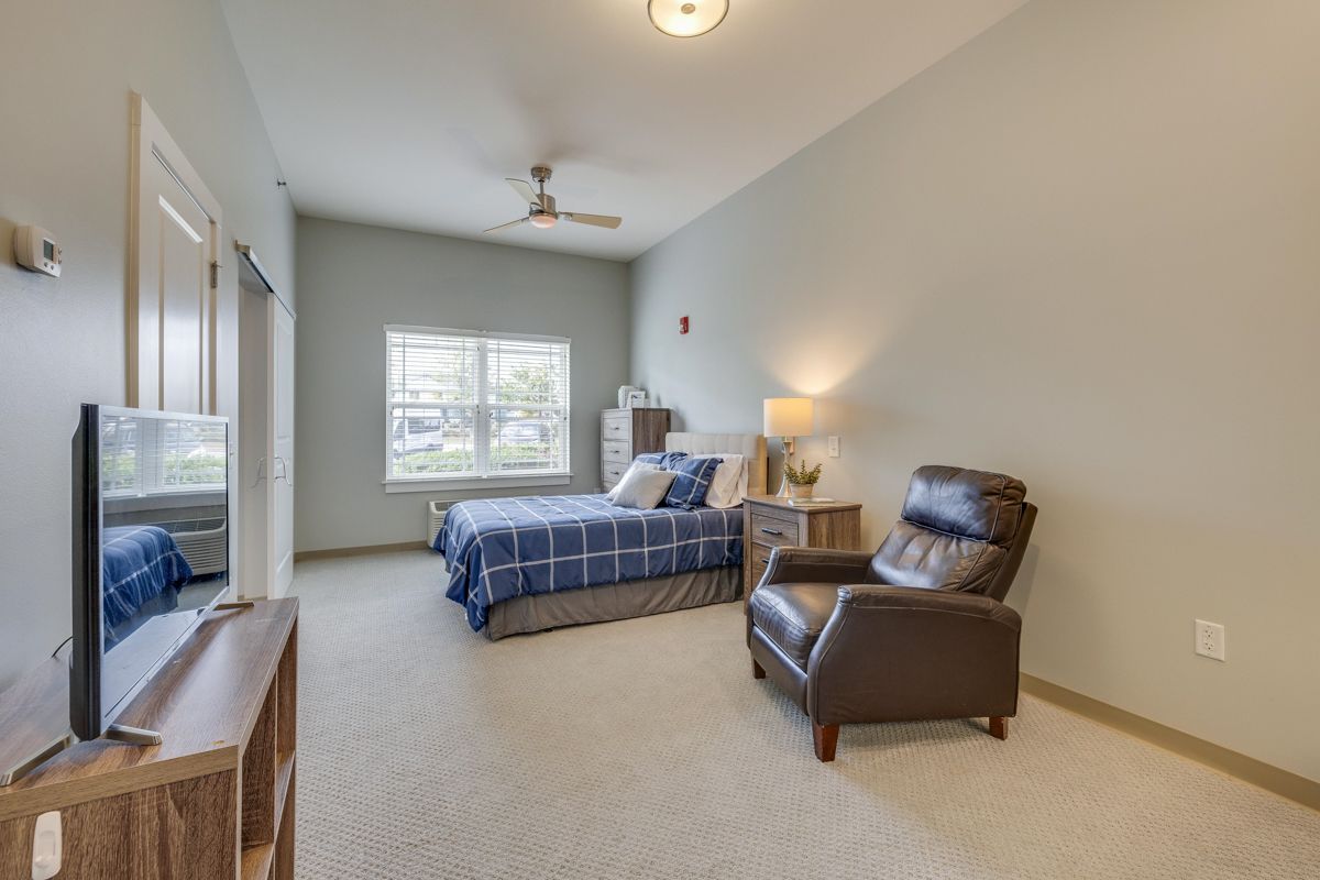 A bedroom with two beds , a chair , a television and a ceiling fan.