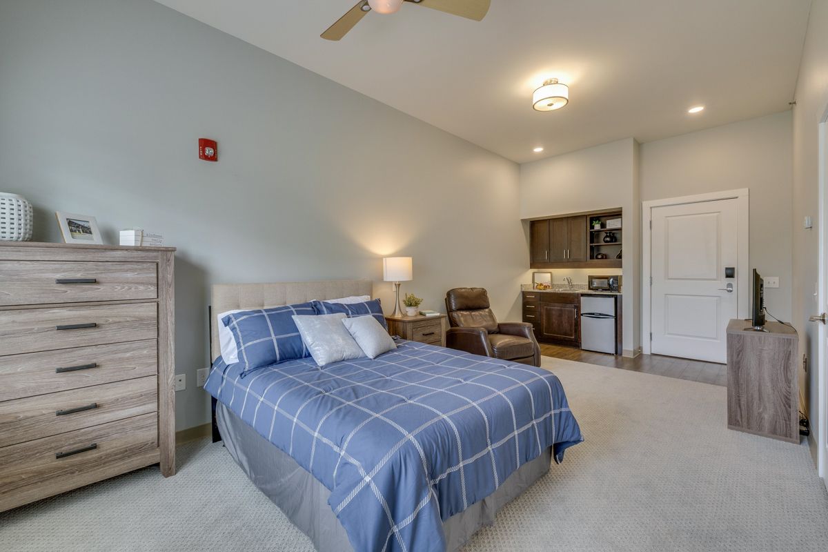 A bedroom with a bed , dresser , chair and ceiling fan.