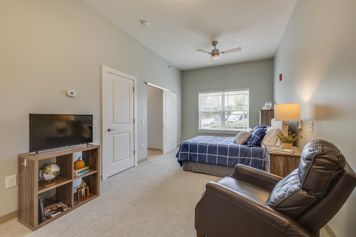 A bedroom with a bed , chair , television and a ceiling fan.
