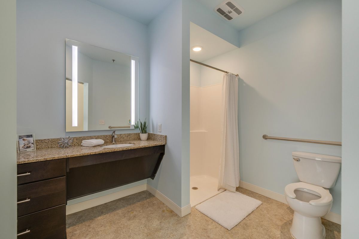 A bathroom with a toilet , sink , mirror and shower.