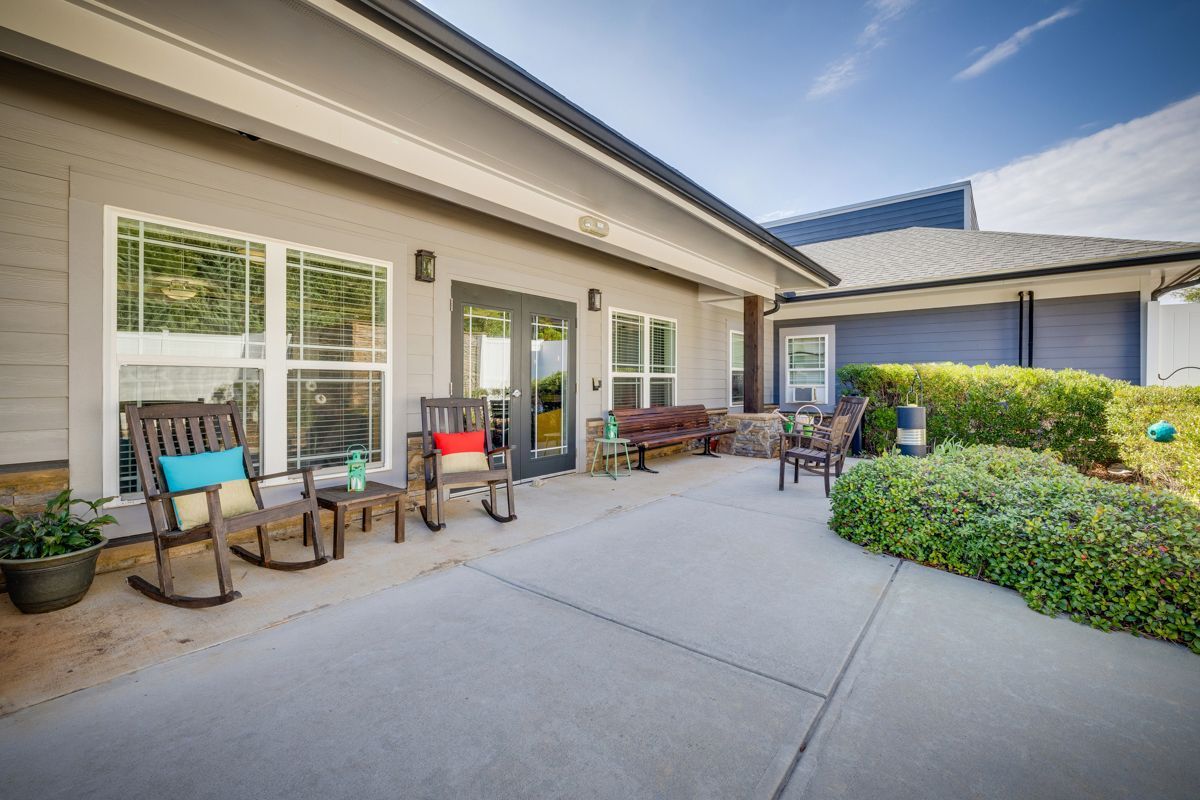 A patio with rocking chairs and tables in front of a house.