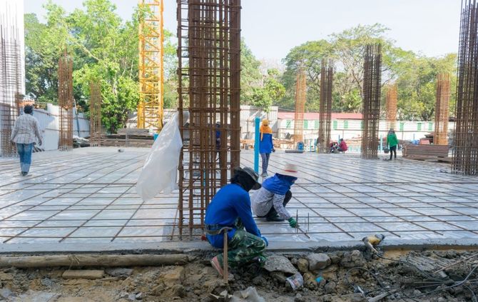 Construction workers pouring concrete around rebar columns at an outdoor building site