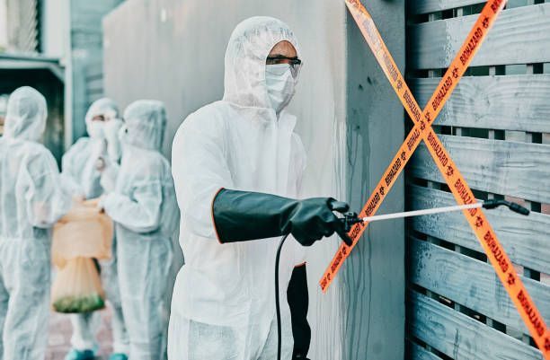 Workers in protective suits disinfecting a building entrance with orange caution tape across the door