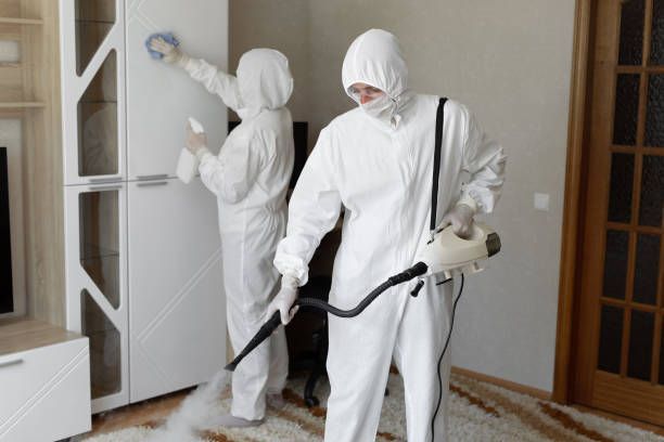 Two workers in white protective suits spraying and cleaning a room indoors