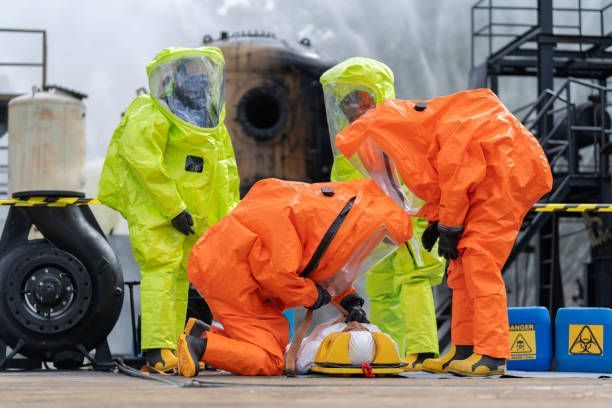 Workers in orange and yellow hazmat suits inspecting equipment near a large industrial pipe.