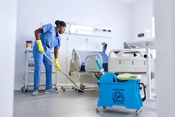 Cleaner mopping a bright hospital room beside a bed and cart