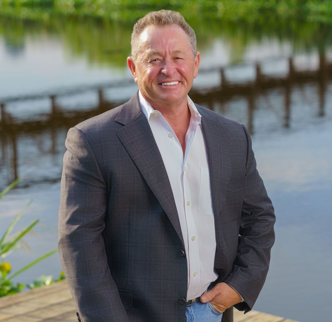 A man in a suit and white shirt is standing on a dock next to a body of water.