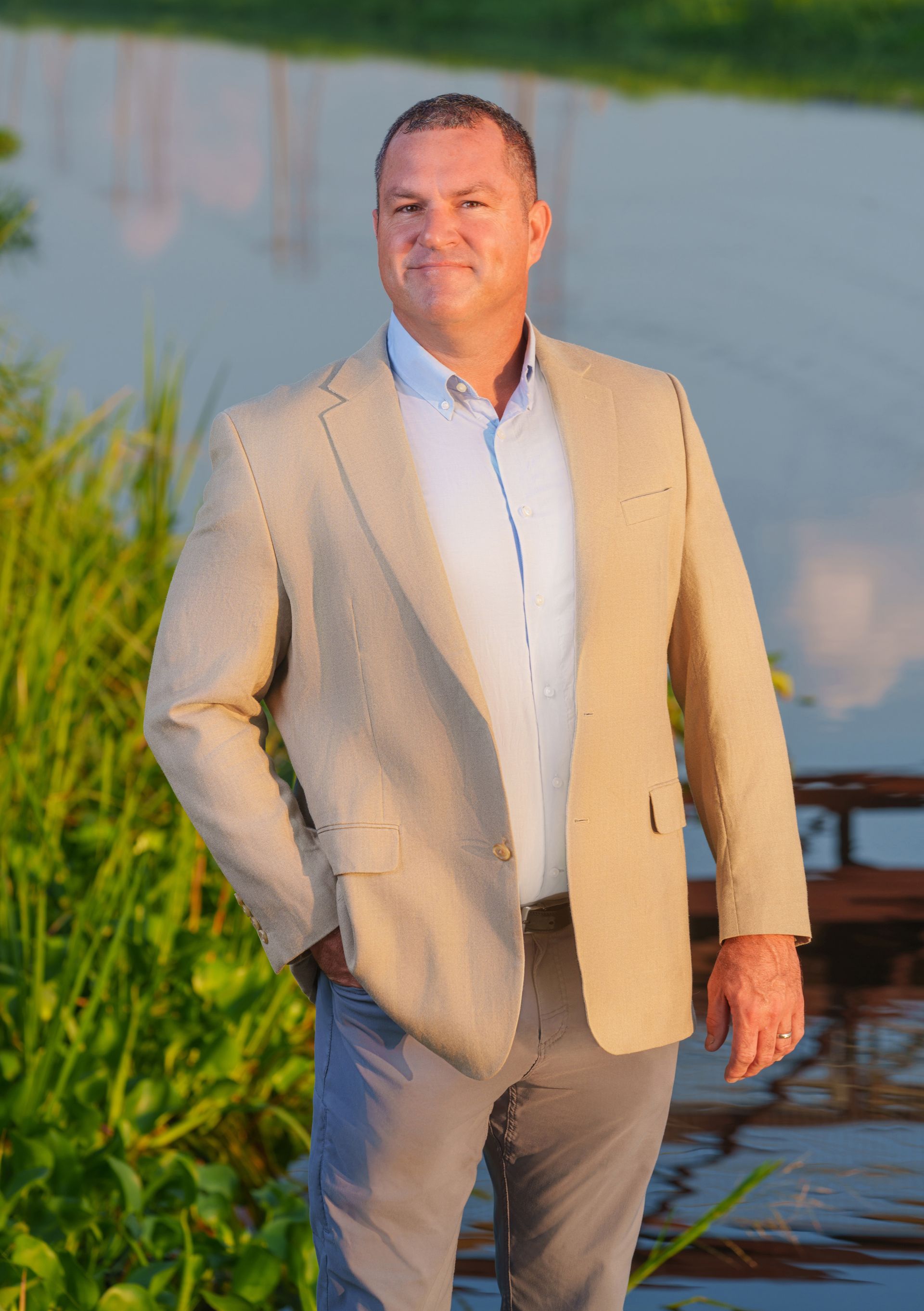 A man in a suit and white shirt is standing on a dock next to a body of water.