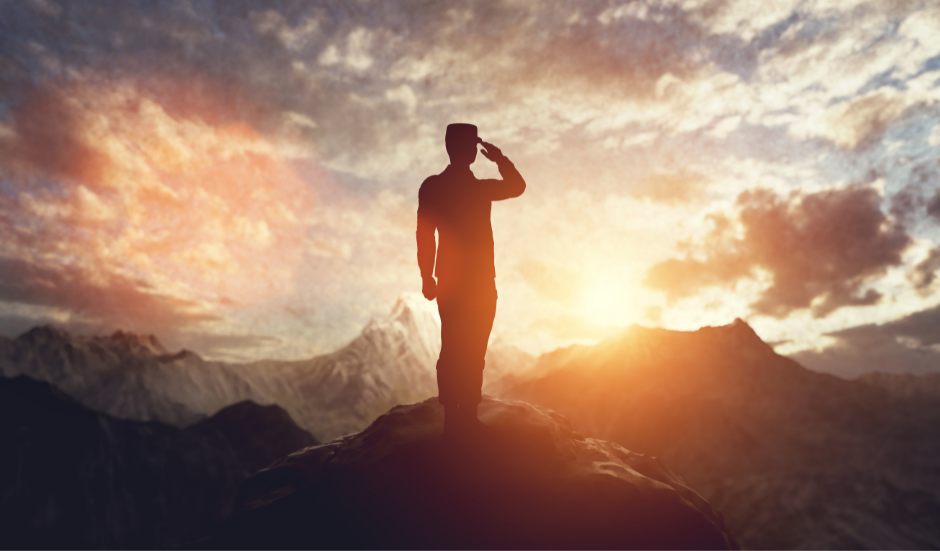 A man is saluting on top of a mountain at sunset.