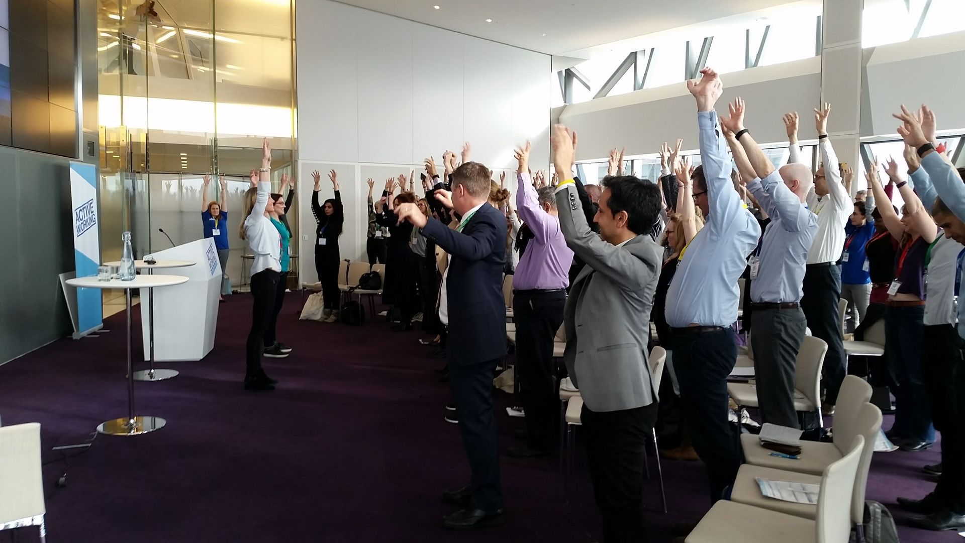 Group of people standing up stretching at a conference or meeting.