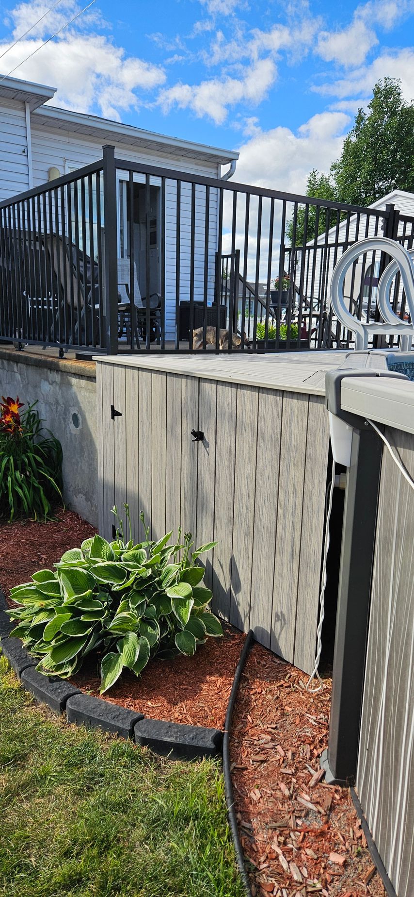 Une terrasse surélevée avec une balustrade noire, construite sur un mur de soutènement. L'aménagement paysager est composé de paillis rouge et de feuillage vert.