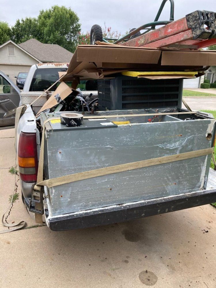 A truck with a lot of junk in the back is parked in a driveway.