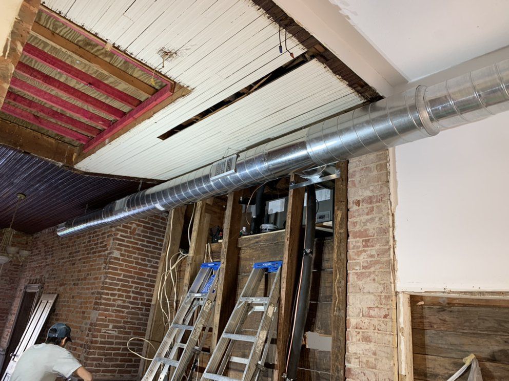 A man is standing in a room with a ladder and a pipe hanging from the ceiling.