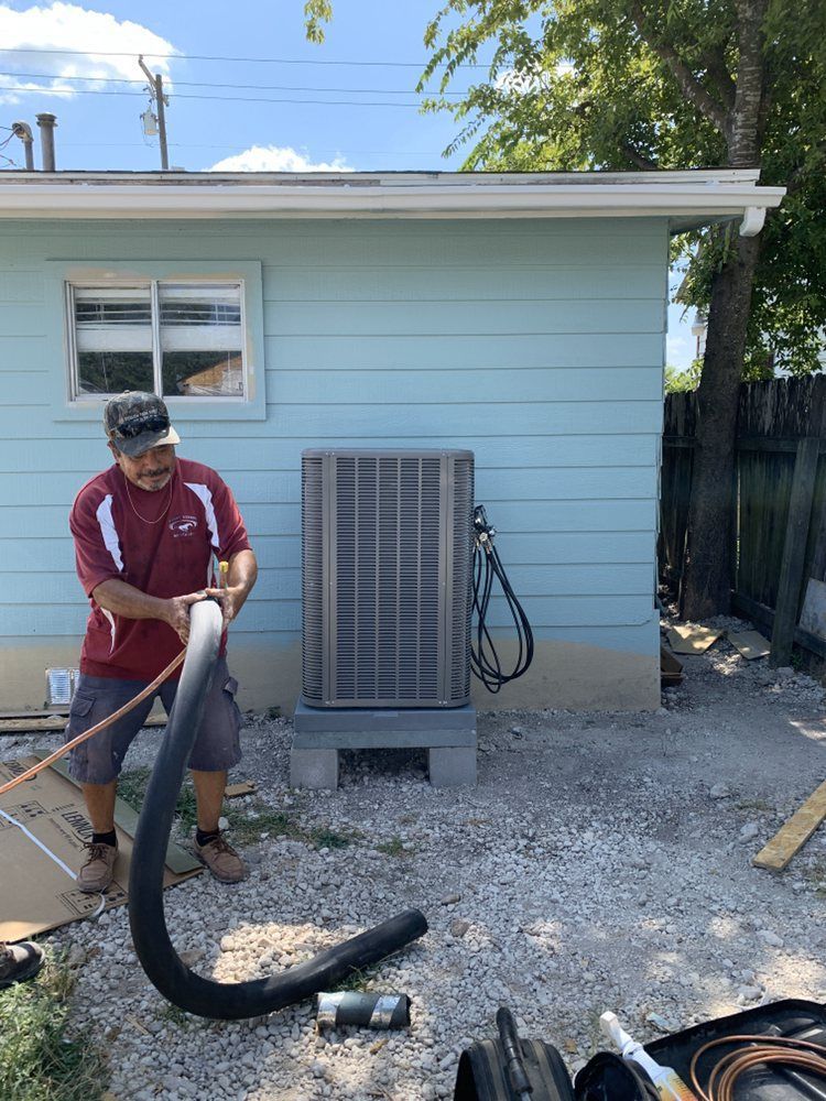 A man is standing in front of a blue house holding a hose.