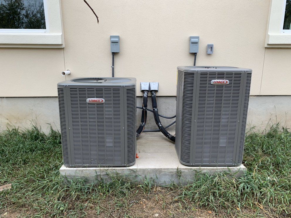 Two air conditioners are sitting next to each other on the side of a house.