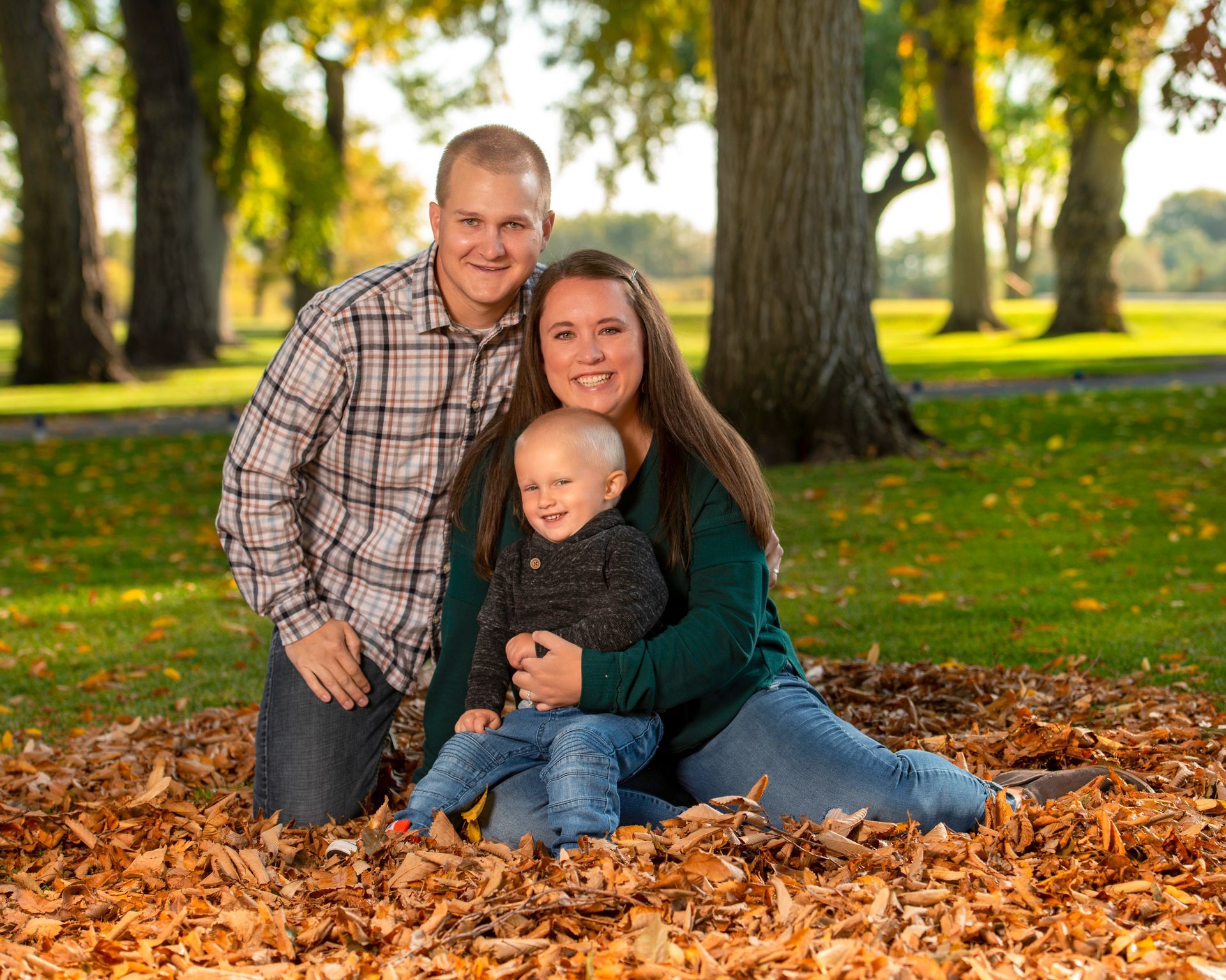 A family is posing for a picture in a pile of leaves in a park.
