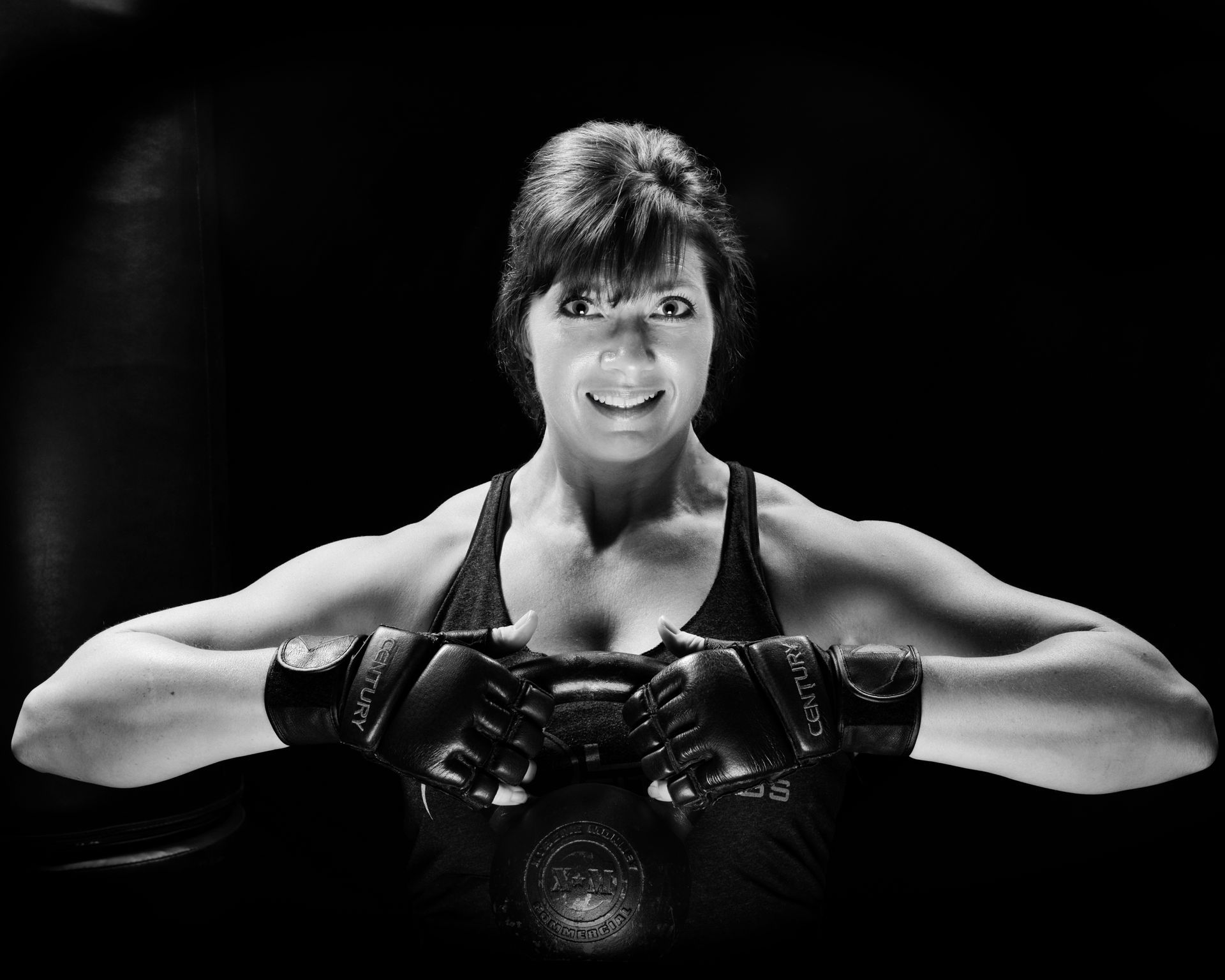 A woman is wearing boxing gloves and smiling in a black and white photo.