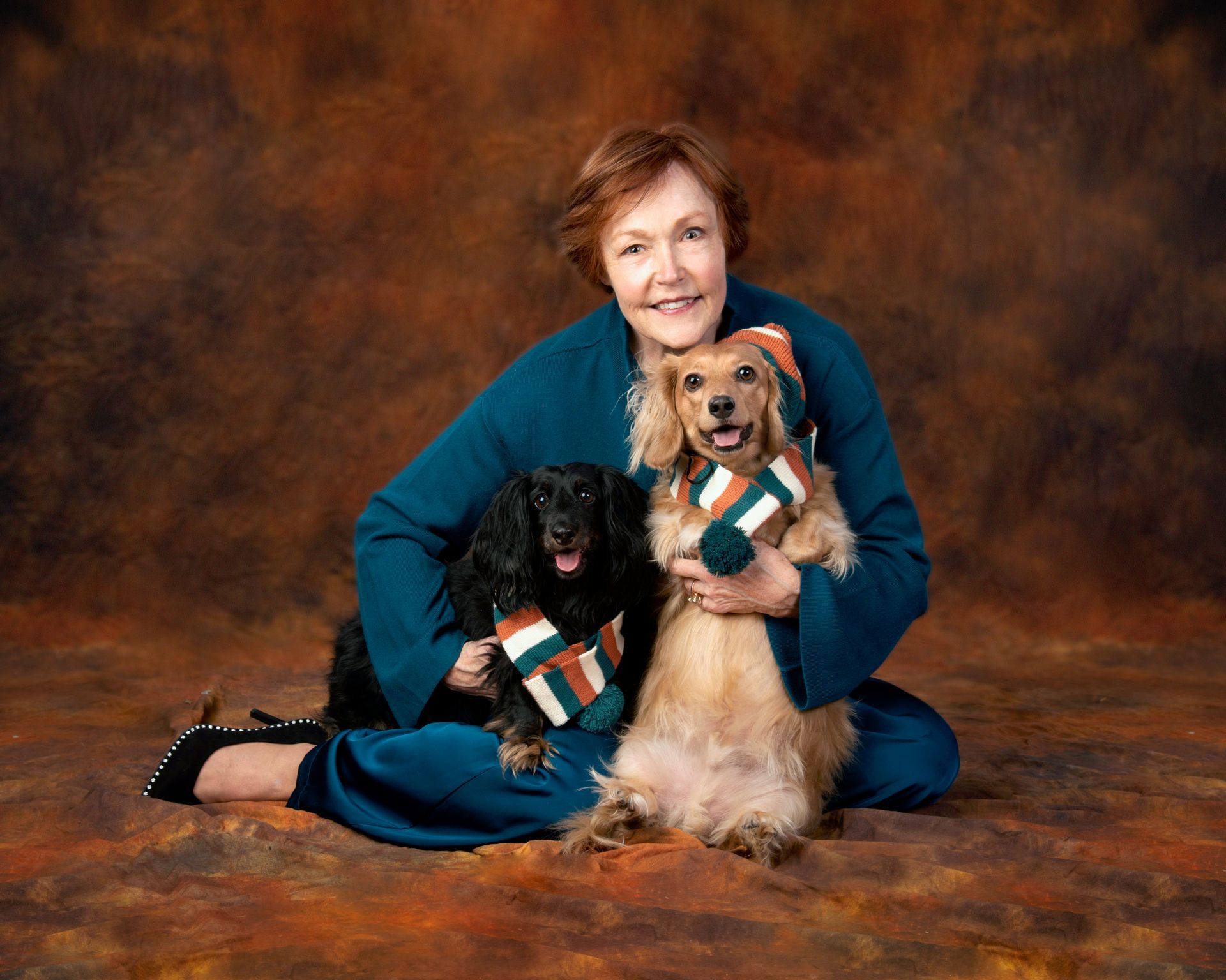 A woman is sitting on the floor with two dogs wearing scarves with the letter t on them