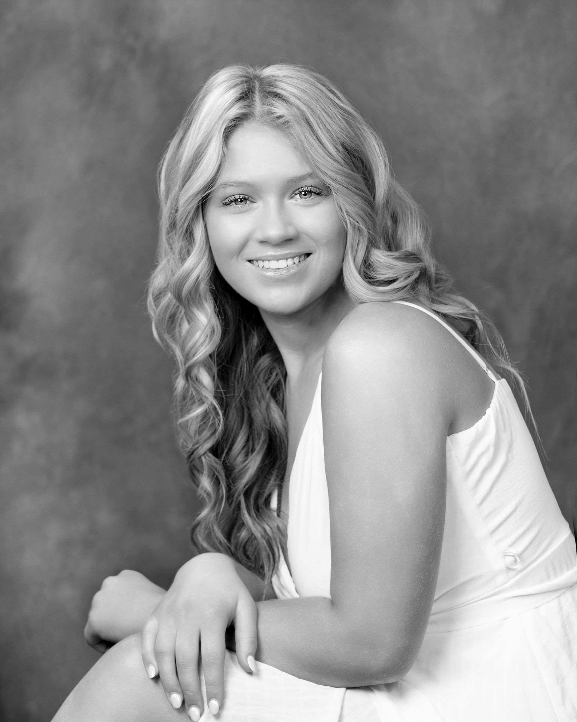 A woman in a white dress is smiling in a black and white photo.