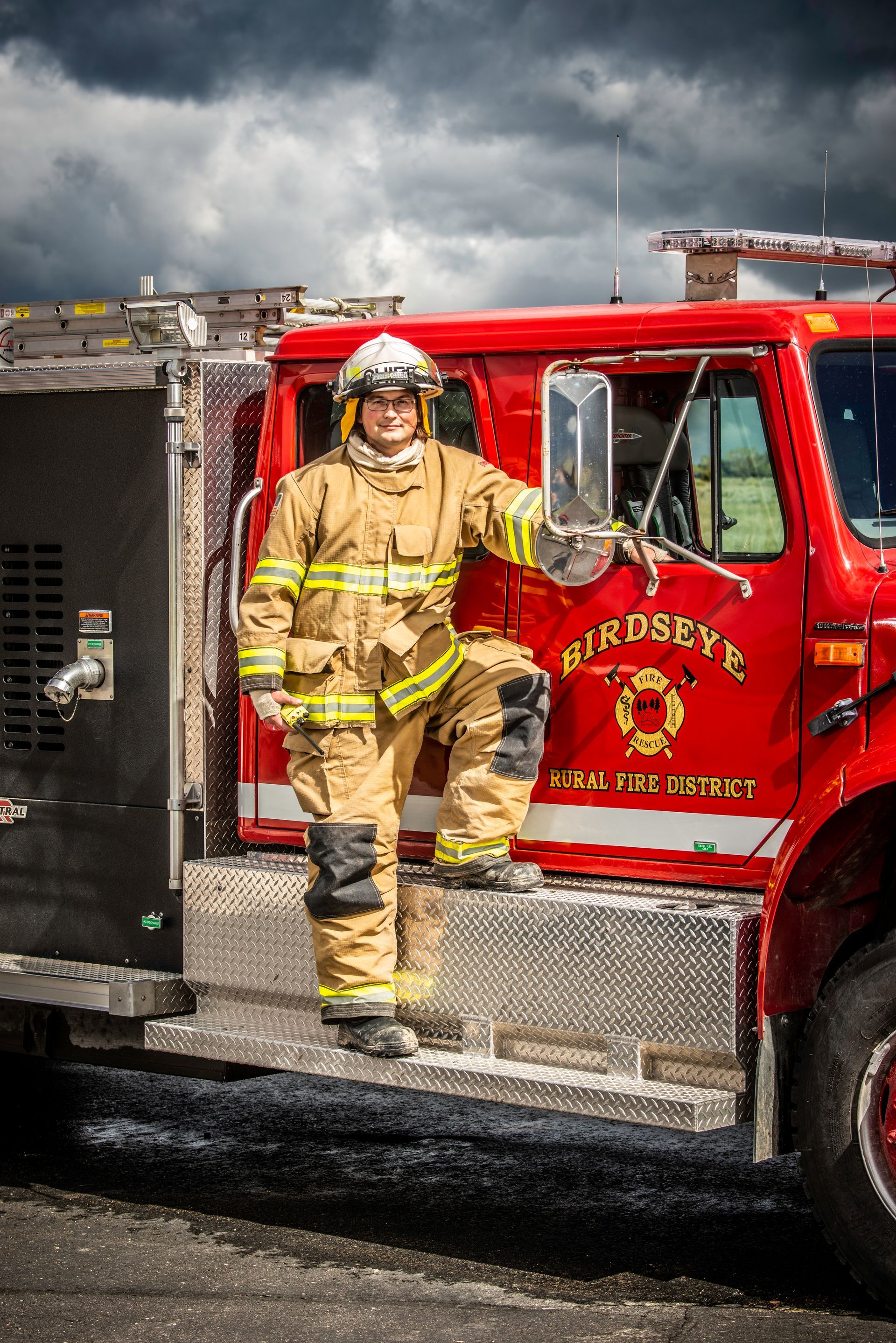 A firefighter is standing on the steps of a red fire truck.
