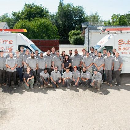 A large group of people are posing for a picture in front of a sub electric truck.