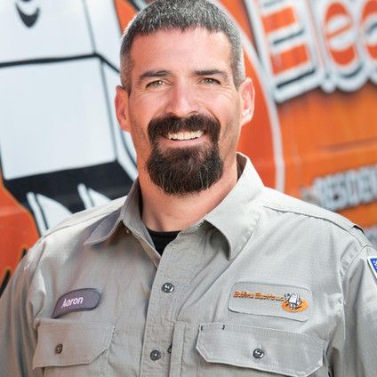 A man with a beard is smiling in front of an orange van.