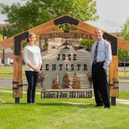 A man and a woman are standing in front of a sign for jose dentistry.