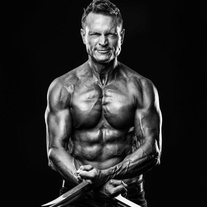 A black and white photo of a shirtless man holding a pair of scissors.