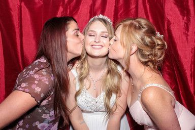 Two women kissing a bride on the cheek in a photo booth.