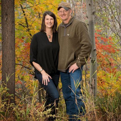 A man and a woman are posing for a picture in the woods.