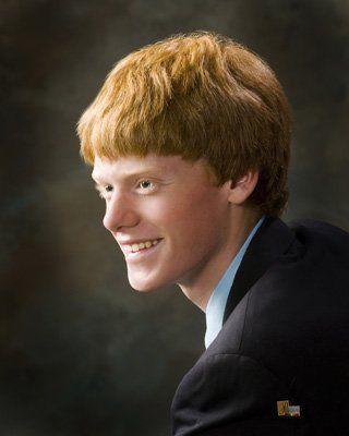 A young man with red hair is wearing a suit and smiling