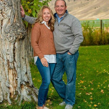 A man and a woman are posing for a picture next to a tree.