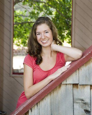 A woman in a red shirt is leaning on a wooden railing.