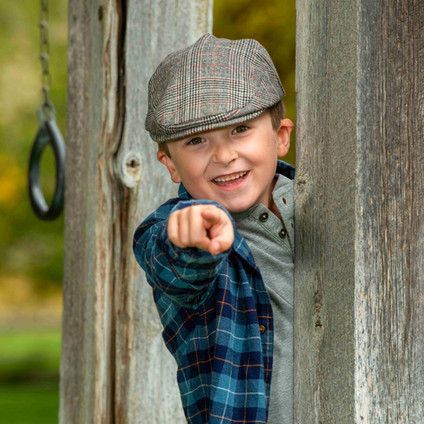 A young boy wearing a hat and plaid shirt is pointing at the camera.