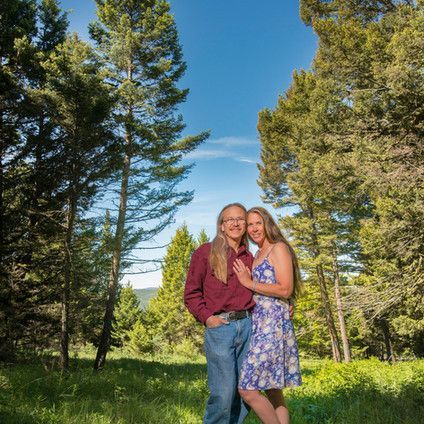 A man and a woman are standing in a field with trees in the background.