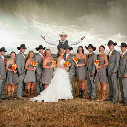 A bride and groom pose with their wedding party in a field.
