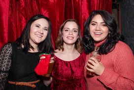 Three women are posing for a picture in front of a red curtain.