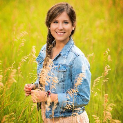 A woman in a denim jacket is standing in a field of tall grass.
