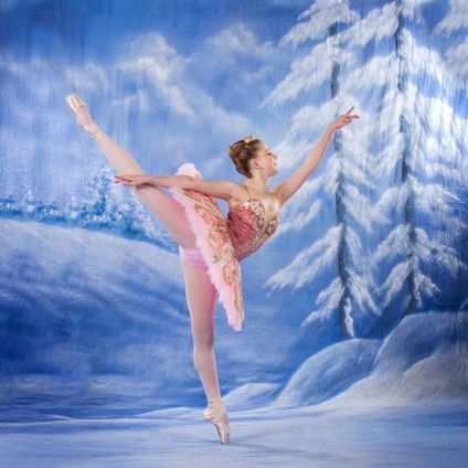 A ballerina is standing on one leg in front of a snowy forest.