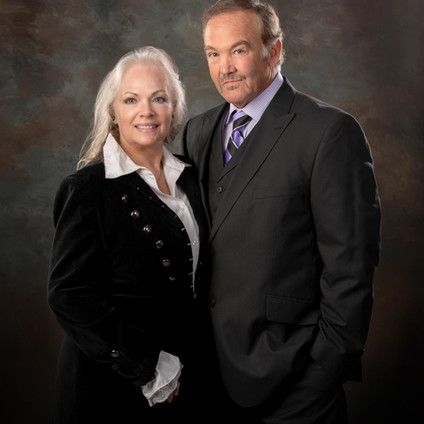 A man in a suit and tie is standing next to a woman in a black jacket.