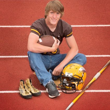 A young man is sitting on a track holding a football and a helmet