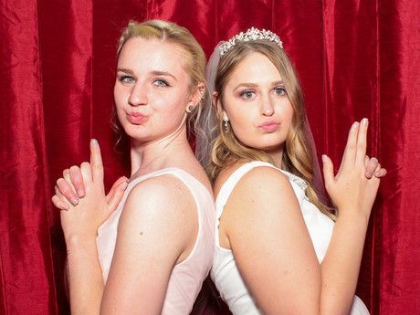 Two women in wedding dresses are posing for a picture in a photo booth.