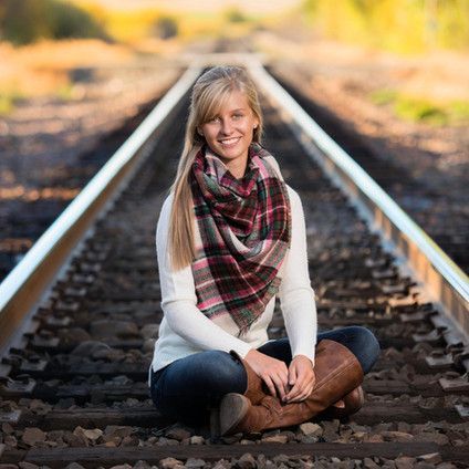 A woman is sitting on train tracks wearing a scarf and boots.