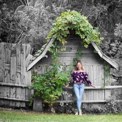 A woman is standing in front of a wooden house with ivy growing on it.
