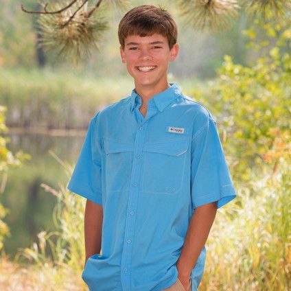 A young boy wearing a blue shirt is standing in a field with his hands in his pockets.