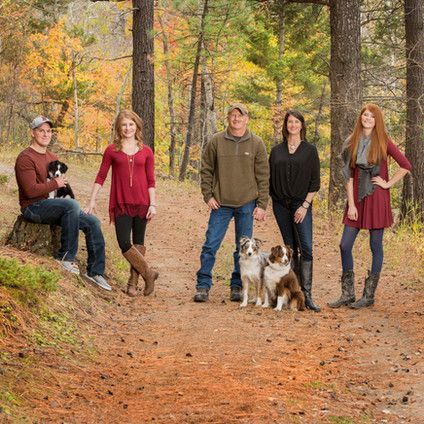 A family is posing for a picture in the woods with their dogs.